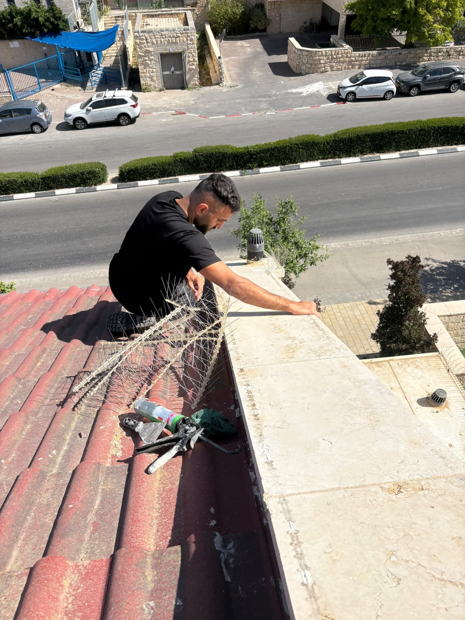 טכנאי של יונה אאוט מתקין רצועת דוקרנים על קיר הגדר בקצה גג רעפים